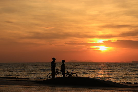 The silhouette of a couple riding a bike to see the sunrise on the beach at morning