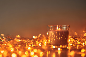 Burning candle with a golden garland lights in bokeh on dark background