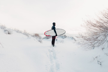 Cold winter and surfer with surfboard. Snowy day with surfer in wetsuit.