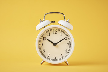 White retro alarm clock on the yellow background with copy space. Time concept