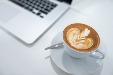 Close up of Latte art coffee cup with keyboard of laptop computer