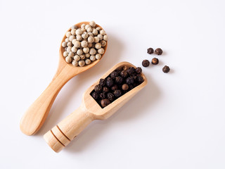 Close-up of black pepper and white pepper in wooden spoon isolated on white background.
