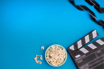 Clapper board with popcorn and film strip on a bright blue background with copy space. For articles about the movie.