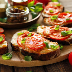 Caprese toast ( bruschetta), grilled slices of sourdough bread with mozzarella cheese, tomatoes, fresh basil and olive oil on a wooden board, close up. A delicious appetizer