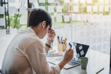 Businessman taking off glasses, feel tired from long hours working on laptop in the office.