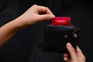 Closeup woman hand holding black Leather Wallet with a red condom at the black background