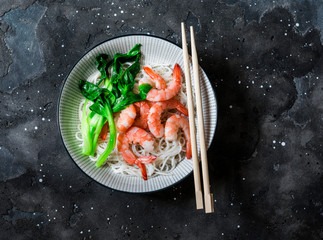 Rice noodles with poached shrimp and bok choy cabbage on a dark background, top view