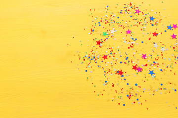 Party colorful confetti over yellow wooden background . Top view, flat lay