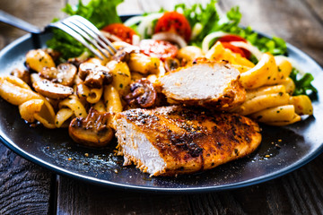 Roast chicken breast with pasta and vegetables on wooden background