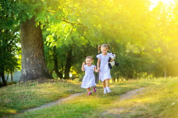 Naklejka na ściany i meble Cute children are walking in the park at sunset. Girls run along the path and have fun. Children play and have fun outdoors.