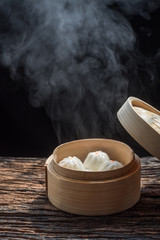 Steam and smoke of hot chinese steamed bun in traditional bamboo steamer on dark...