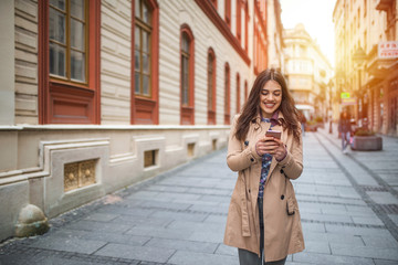 Fototapeta premium Photo of a woman using smart phone. Beautiful woman spending time in the city. Smiling young woman walking outdoors at urban setting and checking messages.