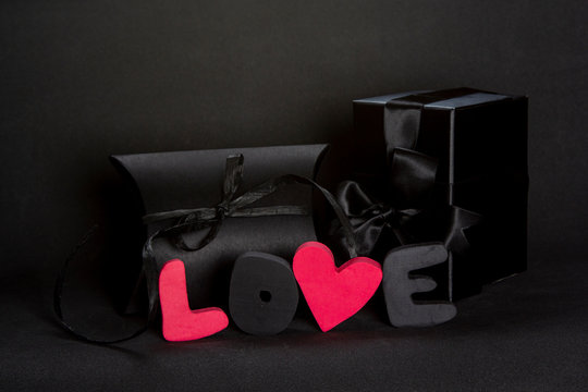 Black gift box and red word LOVE on dark background, copy space. Valentine's day, birthday romantic concept, greeting card.