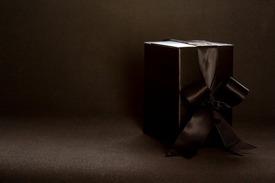 Black gift box with black ribbon bow on dark background, copy space. Valentine's day, birthday romantic concept, greeting card.