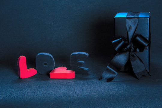 Black gift box and red word LOVE on dark background, copy space. Valentine's day, birthday romantic concept, greeting card.