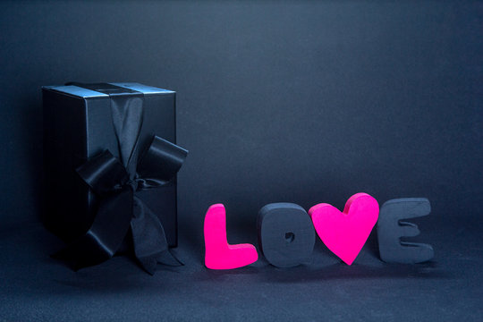 Black gift box and red letters LOVE on dark background, copy space. Valentine's day, birthday romantic concept, greeting card.