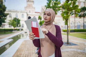 Portrait of beautiful young solo Muslim traveler exploring the city with viewing map on her tablet