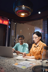 Vertical portrait of two ethnic business people working late in dark office, copy space