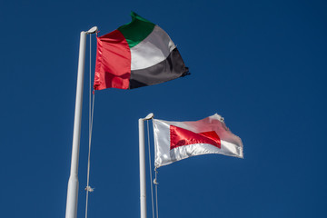 Ras al Khaimah flag (red and white) in the United Arab Emirates (UAE) north of Dubai, and  UAE flag blowing in the wind on a blue sky background.