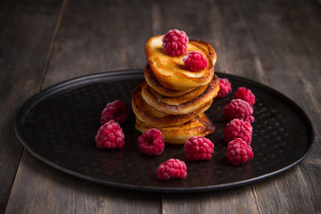 Pancakes with raspberries on a black and wooden background.