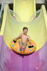 Cute boy sliding on the floater down slide in waterpark. He enjoying his summer vacations.