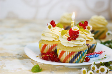 Gentle, festive cupcake with cream and berries nd a candle a light background
