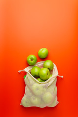 Green apples in a mesh grocery bag on a red background. Flat lay, copy space. Zero waste and no plastic concept.