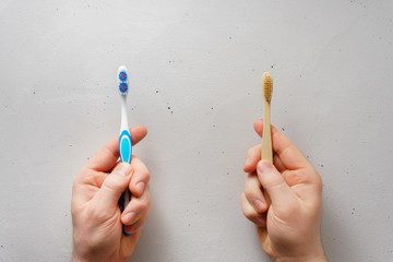 Male hands hold toothbrushes on a light gray concrete background, top view. Choose between plastic and bamboo toothbrush. No plastic concept.