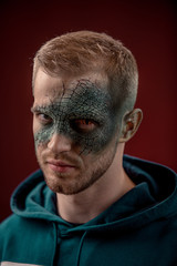 man with professional horror movie make-up green lizard on dark red background. lizard eye