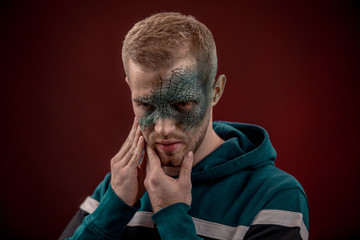 man with professional horror movie make-up green lizard on dark red background. lizard eye