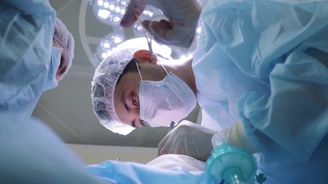 A surgeon and an assistant perform an operation on a patient. Sew a wound. Hands in blood