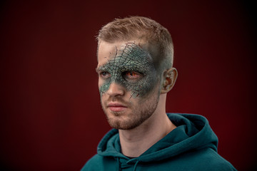 man with professional horror movie make-up green lizard on dark red background. lizard eye
