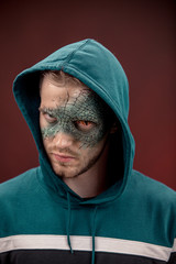 man with professional horror movie make-up green lizard on dark red background. lizard eye