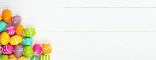 Colorful Easter banner with corner border of Easter Eggs against a white wood background. Top view with copy space.