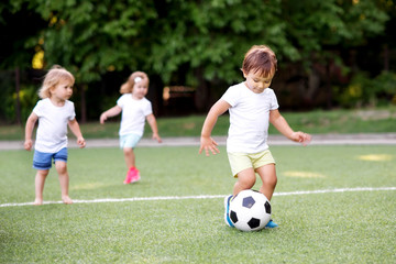 Football game: team of toddlers playing soccer on green field: three children, two boys (one is...