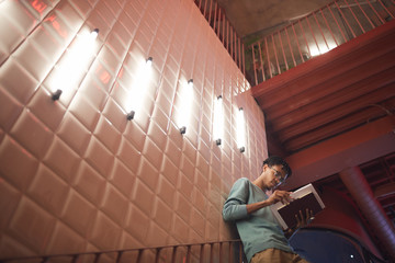 Wide angle portrait of young African-American man holding books while leaning on wall in college campus, copy space