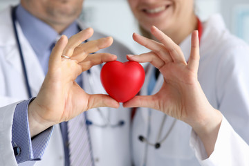 Doctors in white coats hold heart, focus on heart. Male and female doctors in white coats are...