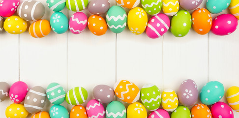 Colorful Easter banner with double border of Easter Eggs against a white wood background. Top view with copy space.