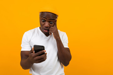 handsome black african man looks in surprise on the phone on a yellow background