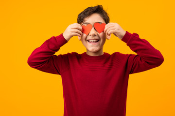 funny handsome Caucasian boy with two paper cards in the form of hearts for Valentine's Day on an orange background