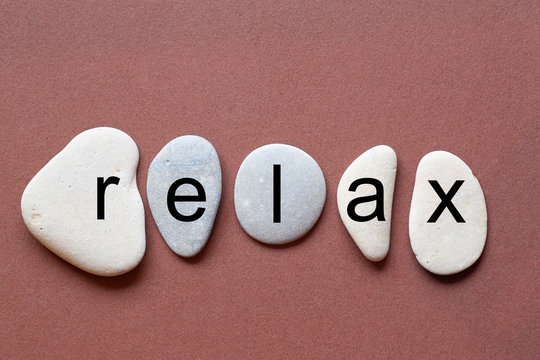 relax as a word on flat stones in natural color and shape. A letter in black color on each stone isolated against a brown background