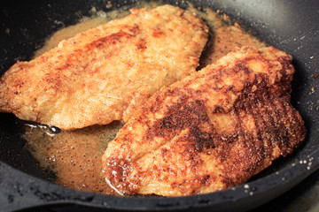 Tilapia fish fillets rolled in flour and breadcrumbs to roast in pan.
