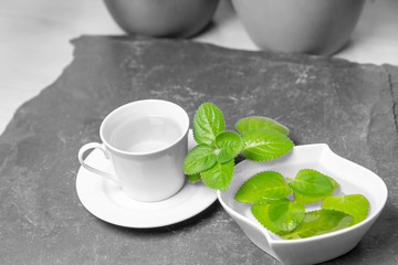 Cup of Silver Spurflower tea and leaves in a white bowl on stone slate plate.  Color Splash Effect Photo.