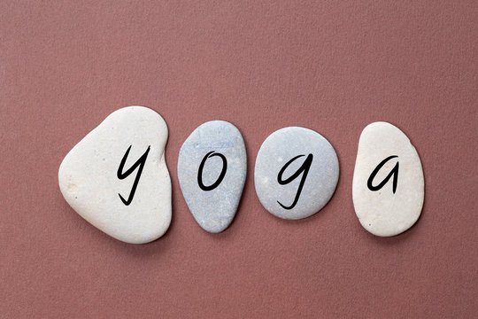 yoga as a word on flat stones in natural color and shape. A letter in black color on each stone isolated against a brown background
