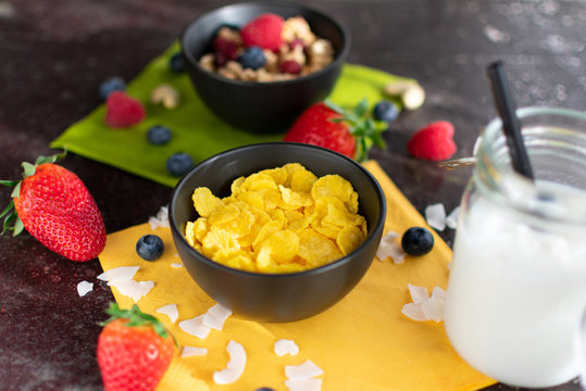 Schüssel mit leckeren Cornflakes. Dazu Kokosmilch und Müsli unscharf dargestellt