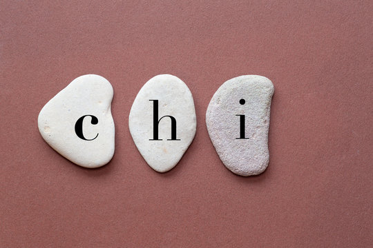 chi as a word on flat stones in natural color and shape. A letter in black color on each stone isolated against a brown background