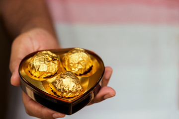 Man Giving Chocolate. Valentines day gift background with copy space. Young male hand holding & giving heart shaped luxury chocolate box. Concept for couple love, romance, birthday, wishing card.