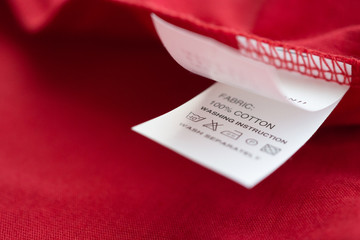 Fototapeta premium White laundry care washing instructions clothes label on red cotton shirt