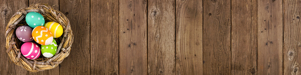 Nest with colorful Easter Eggs. Banner orientation over a rustic old wood background. Above view...