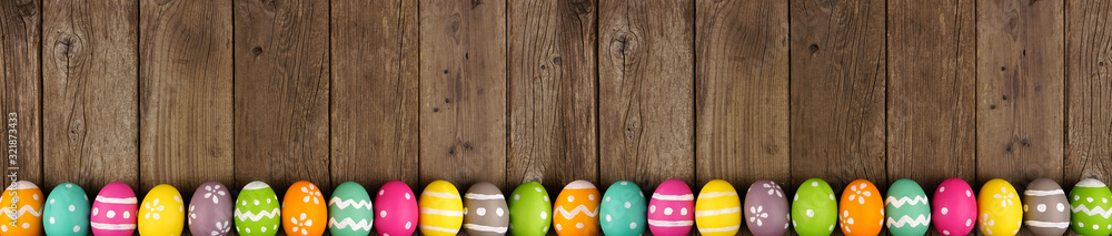 Poster Colorful Easter banner with row of eggs bottom border over a rustic old wood background. Top view with copy space.